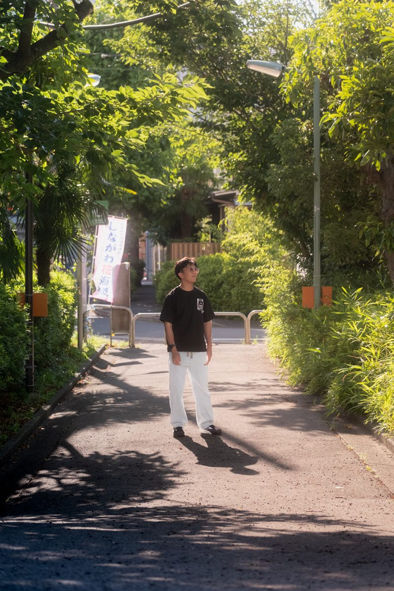 Damien standing on a sunlit, tree-lined path